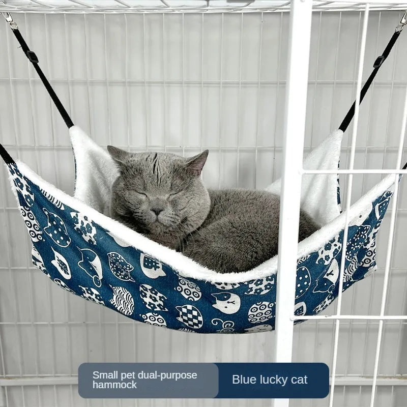 Eine graue Katze entspannt sich in einem blau gemusterten Hamax, der in einem Drahtkäfig hängt.