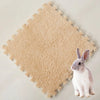 A small gray rabbit sits on a beige, fluffy fleece pet warming mat.