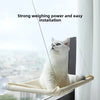 A white cat is resting in a beige hanging hammock window perch with suction cups.