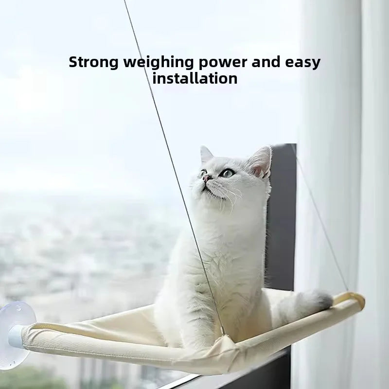 A white cat is resting in a beige hanging hammock window perch with suction cups.