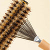 A close-up of a natural wooden hairbrush cleaner with golden bristles and a wooden handle.
