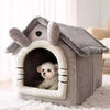 A gray pet house with a textured roof and entrance, featuring a small white puppy inside.