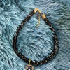 A black beaded collar with a gold chain and a sparkling crystal heart pendant resting on a blue fuzzy surface.