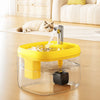 A clear glass cat drinking fountain with a yellow base is shown on a wooden floor, featuring a stream of water.