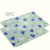 Two light green pet pee pads with purple and pink hearts and clouds