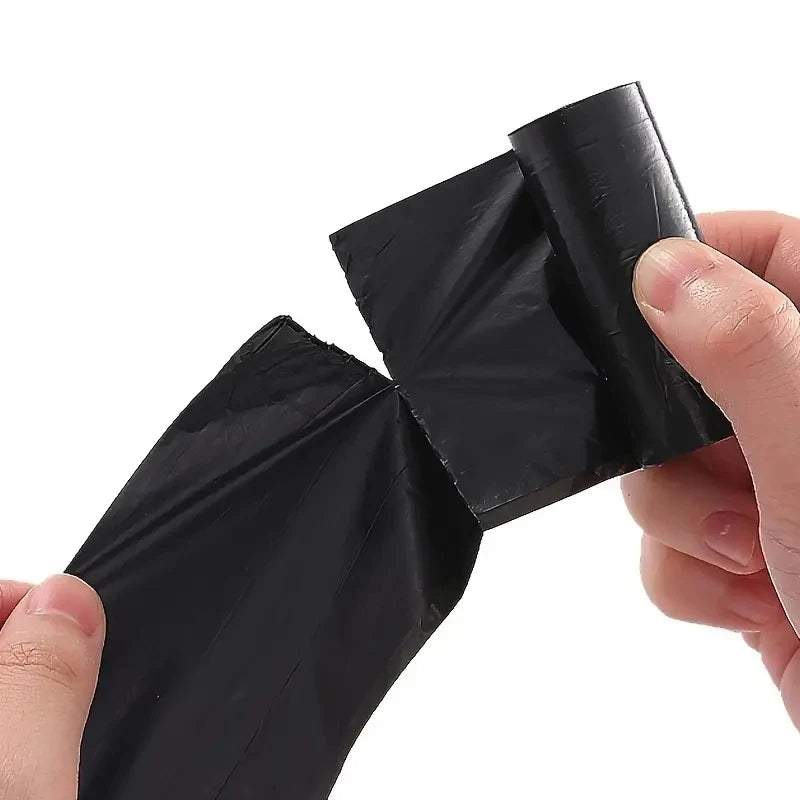 A hand is holding a black biodegradable dog poop bag with an easy-tear design.