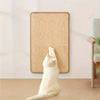 A white cat is scratching on a beige, rectangular cat scratch board mounted on a wall.