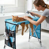 A woman is using a handheld shower to wash a cat inside a blue foldable pet grooming hammock.