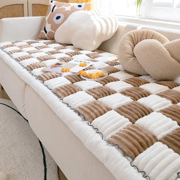 A plush fleece pet bed and mat featuring a beige and brown diamond pattern on a light-colored sofa.