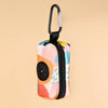A colorful, fabric poop bag holder with a black strap and clip is shown against a light background.