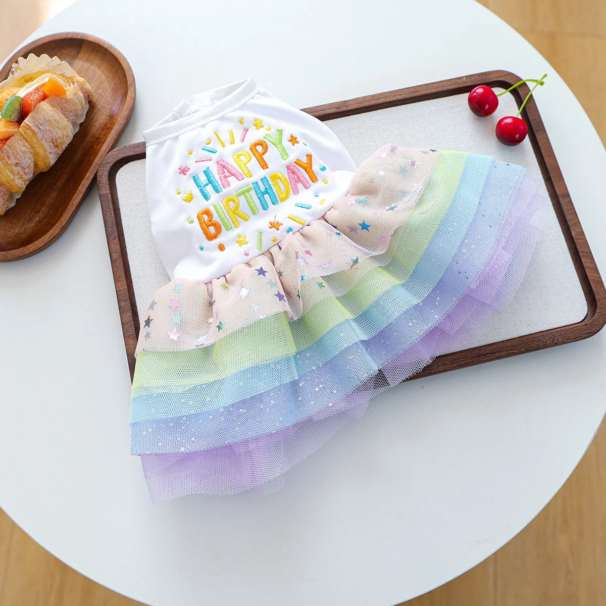 Elegant birthday suit for dogs featuring a white top and colorful tulle skirt on a wooden tray.