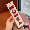 A hand holds a white card displaying five handmade flower-shaped baby hair clips in shades of red and pink.