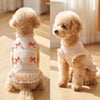 A light beige poodle wearing a yellow and white striped bow dog suit with pink trim.