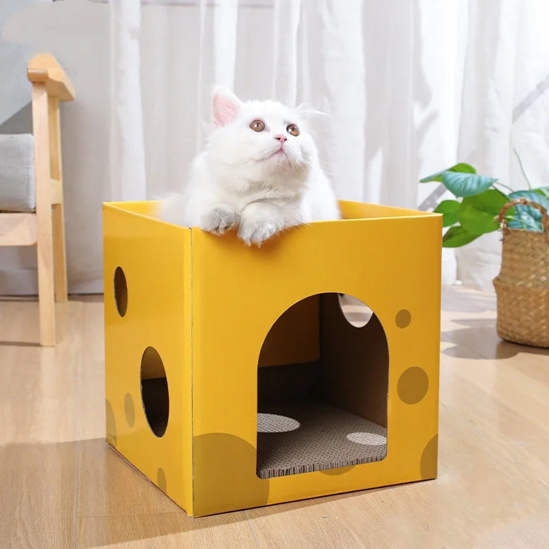 A fluffy white cat is sitting inside a yellow cardboard scratching house with circular cutouts.