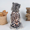 A fluffy gray pet wearing a leopard print vest, sitting next to a loaf of bread.