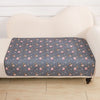 A gray pet pee pad with small pink and white animal designs is placed on a white upholstered surface.