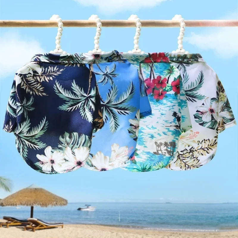 A collection of floral and tropical Hawaiian style pet dog summer beach shirts hanging on a wooden bar against a blue sky and
