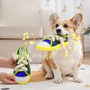 A small dog is holding a yellow squeaky slipper toy with a rope, being presented by a human hand.