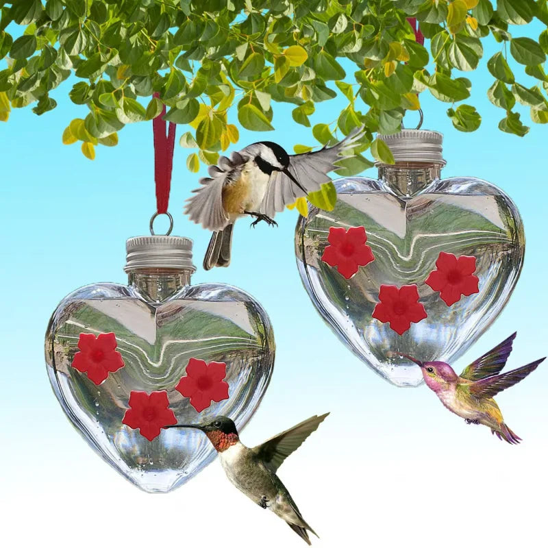 Un distributeur suspendu en forme de cœur en verre rempli d'eau, avec plusieurs colibris perchés sur les feuilles ci-dessus.