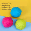 Three rubber chew toys in blue, pink, and yellow are displayed on a light blue surface.