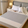 A gray reusable pet training pad is placed on a white bed, surrounded by pillows and a bedside lamp.
