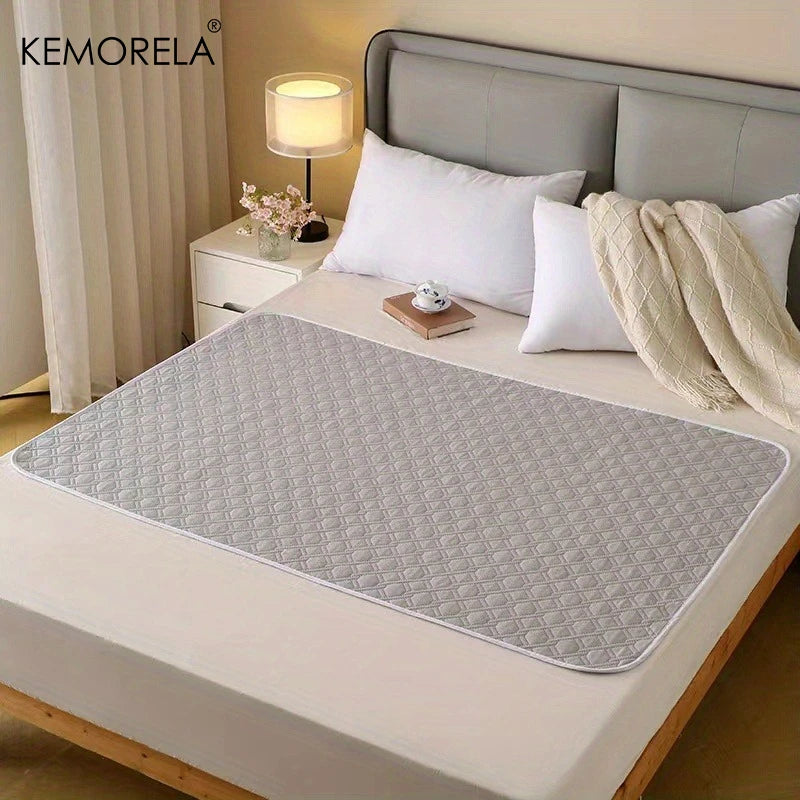 A gray reusable pet training pad is placed on a white bed, surrounded by pillows and a bedside lamp.