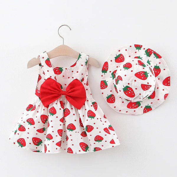 Ein weißes Sommerkleid mit roter Erdbeere-Muster und einer passenden roten Mütze auf einem Bügel.