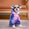 A small dog wearing a tie-dye fleece hoodie with pink and blue colors.