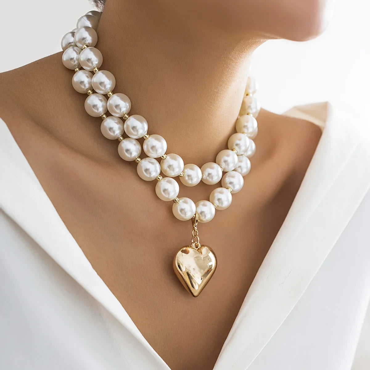 A close-up of a pearl heart pendant choker necklace worn around the neck against a light background.