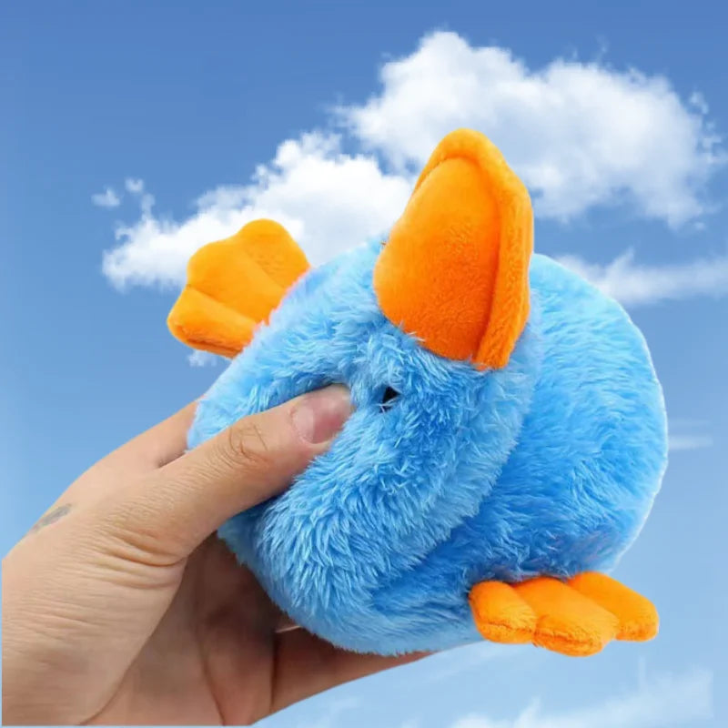 A hand is holding an orange and blue plush duck pet toy against a bright blue sky background.