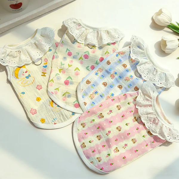 A pink and white cotton dog vest with a lace collar and cartoon print lying on a white surface.