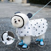Un cachorro blanco con impermeable de lunares negros, parado afuera bajo la lluvia.