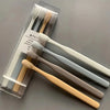 A clear plastic case holds a set of four soft-bristle travel toothbrushes in various natural wood and white colors.