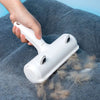 A hand is using a white reusable pet hair remover brush with suction on a gray fabric.