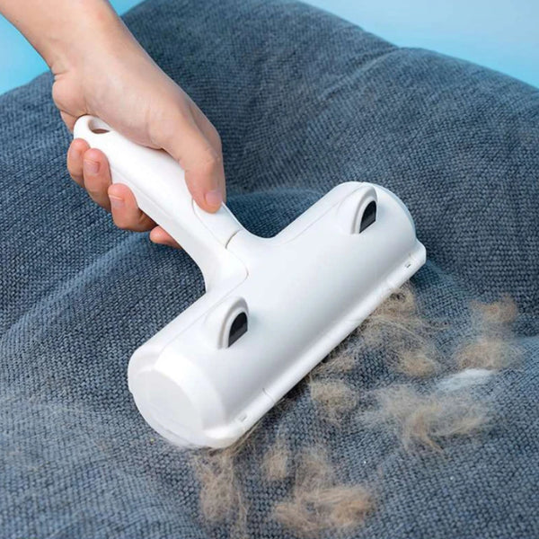 A hand is using a white reusable pet hair remover brush with suction on a gray fabric.