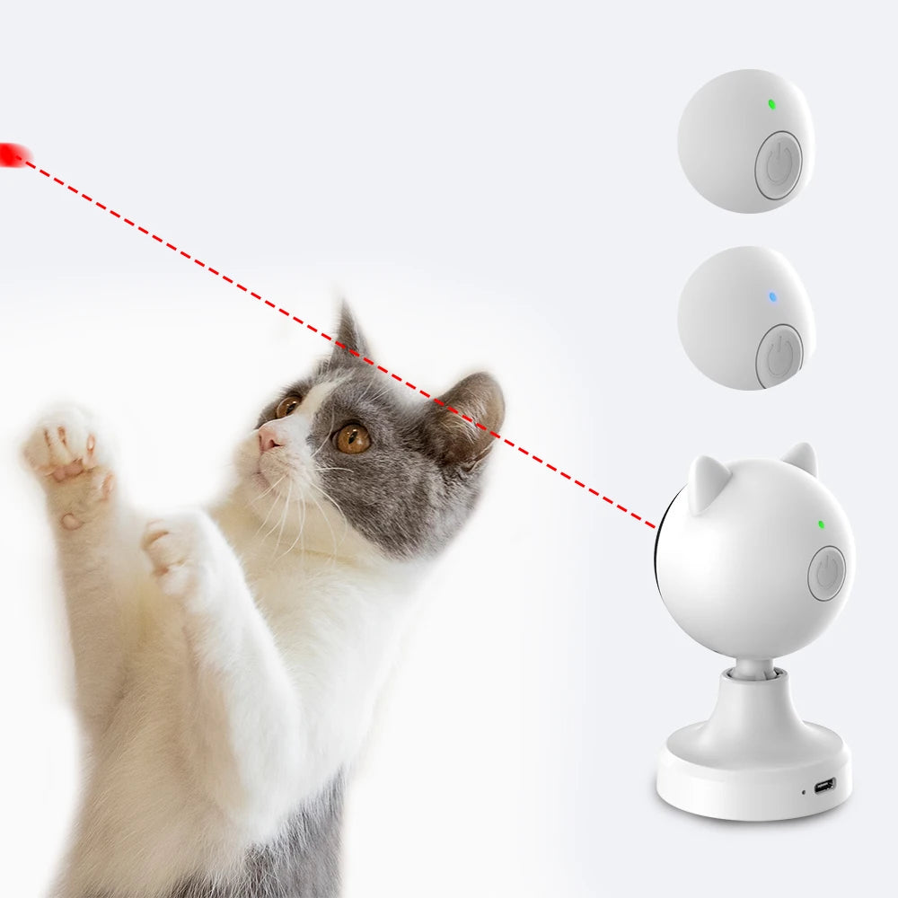 A domestic cat is interacting with an automatic laser toy, which is a white device with a green light.