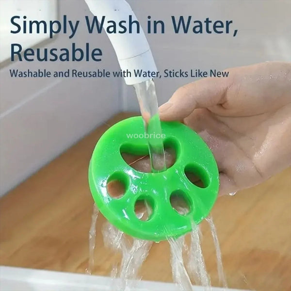A hand is using a reusable green silicone brush to wash pet hair in water.