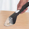 A hand holds a black portable handheld insect catcher with a clear glass-like tip on a wooden surface.