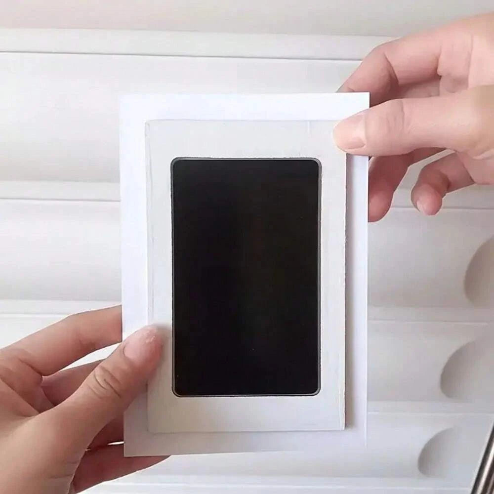 A hand holds an inkless pet paw print kit with a black square impression on a white card.