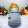 A fluffy grey dog hoodie with a golden fur hood resting on a white surface surrounded by orange and green floral arrangements