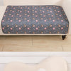 A gray pet pee pad with a repeating pattern of small pink and orange animal figures is placed on a light wooden floor.