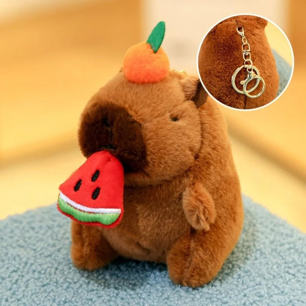 A brown capybara plush toy with an orange fruit on its head and a slice of watermelon attached to its side.