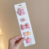 A hand holds a white card displaying five pink and yellow flower-shaped baby hair clips.