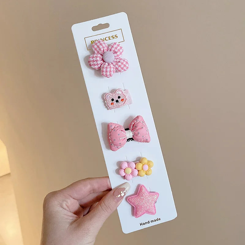 A hand holds a white card displaying five pink and yellow flower-shaped baby hair clips.