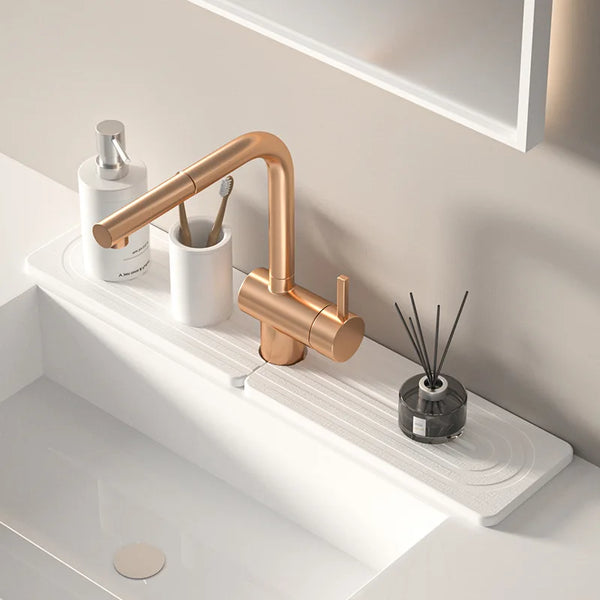 A modern brass faucet mounted on a white countertop next to a bottle and a mat.