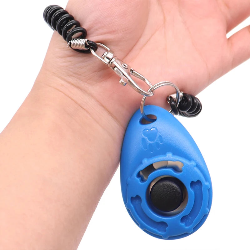 Eine Hand hält einen verstellbaren Hundetrainer-Klicker mit blauem ovalem Körper und schwarzer Nase.