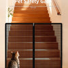A foldable metal mesh pet safety gate installed on a wooden staircase, with a cat looking through the barrier.