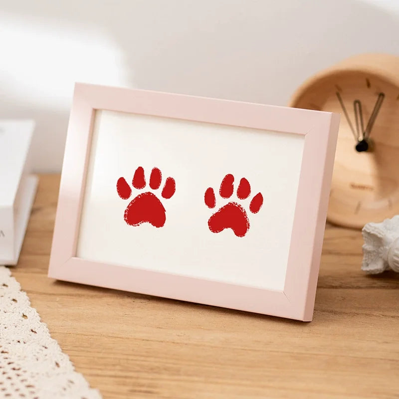 A pink wooden photo frame displaying two red paw prints on a light background.