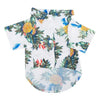 A white dog shirt featuring a tropical Hawaiian leaf print design in shades of green, blue, and yellow.