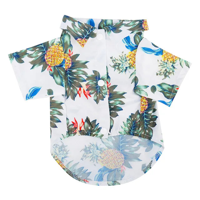 A white dog shirt featuring a tropical Hawaiian leaf print design in shades of green, blue, and yellow.